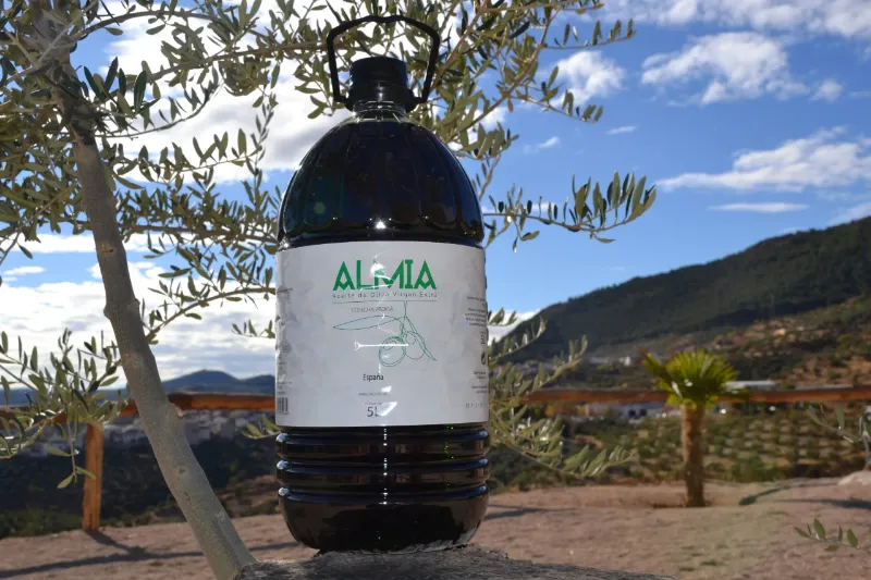 Garrafa de Almia de 5 litros bajo un olivo, con el olivar de Cabra del Santo Cristo detrás